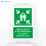 Знак пожарной безопасности с зеленым фоном как символ безопасности и белыми символами E007 «Место сбора при эвакуации», который используется для указания места, куда должны направляться люди в случае эвакуации здания или территории.