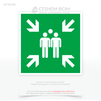 Знак пожарной безопасности с зеленым фоном как символ безопасности и белыми символами E007 «Место сбора при эвакуации», который используется для указания места, куда должны направляться люди в случае эвакуации здания или территории.